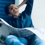 A young South Asian man casually reading a newspaper outdoors in Ernakulam, India.